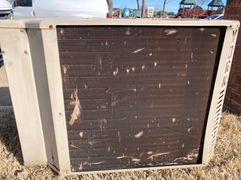 An air conditioning unit badly damaged by hail